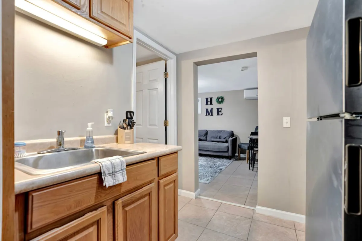 A cozy kitchen area with a sink, wooden cabinets, and an open doorway leading to the living room. The layout is inviting and practical, ideal for preparing quick meals between work sessions or enjoying downtime with friends.