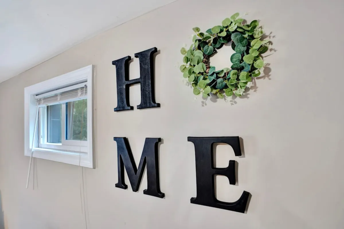 The image shows the word 'HOME' spelled out with decorative letters and accented by a lush green wreath, placed against a neutral backdrop. The scene radiates a sense of warmth and belonging, suggesting a welcoming environment for memorable experiences.