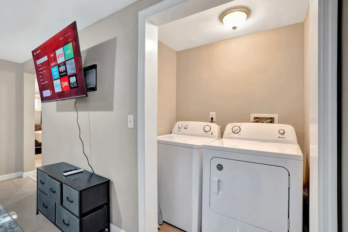 A bright, efficient laundry area featuring a modern washing machine and dryer, with additional touches like a TV and storage unit. The space feels organized, contemporary, and practical for travel convenience.