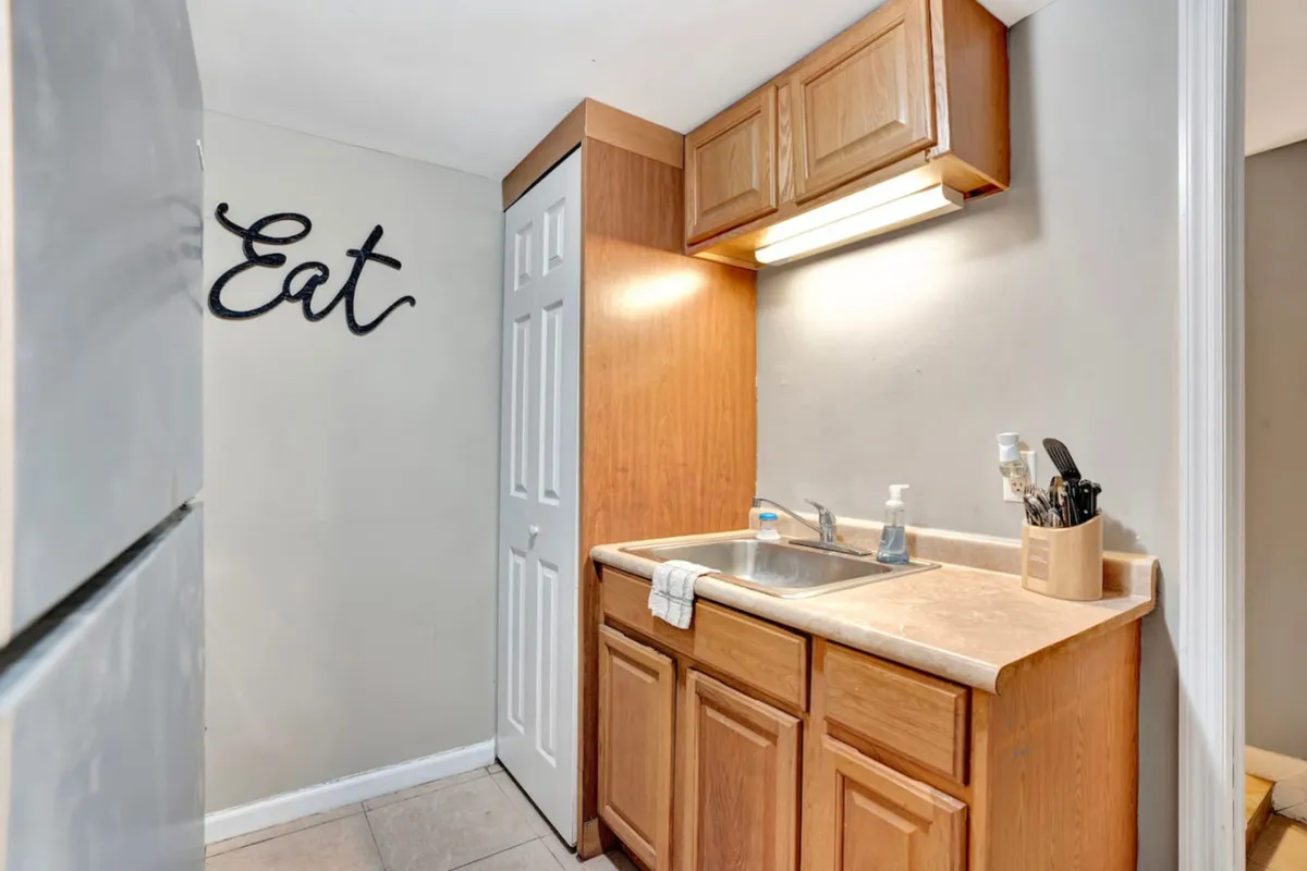 A cozy, functional kitchen interior with wooden cabinets, a sink, kitchen utensils, and a decorative 'eat' sign. The scene evokes a warm, inviting atmosphere ideal for preparing meals, sharing recipes, or celebrating over intimate dinners—highlighting the self-catering aspect mentioned in the section.