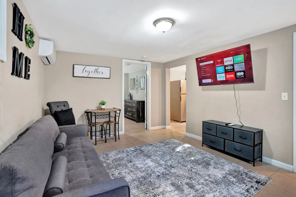 A welcoming open-concept living area featuring a comfortable sofa, dining table, TV, a cozy rug, and decorative wall art. The space is infused with natural light, inviting guests to relax, dine, and socialize in a harmonious setting.