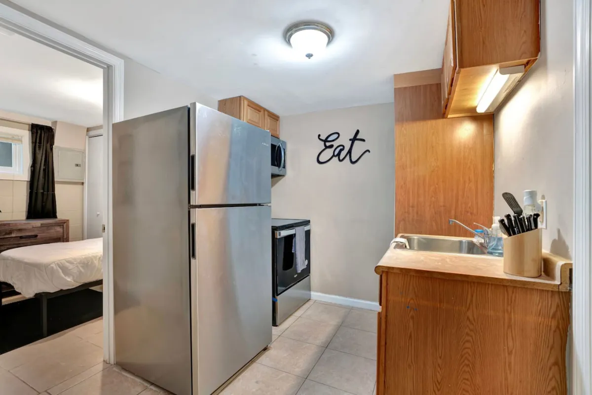 A cozy kitchen setting with a stainless steel refrigerator, kitchen sink, and prominent 'Eat' wall art. The space looks organized and welcoming, with well-placed utensils and counter space for meal preparation or casual conversation.