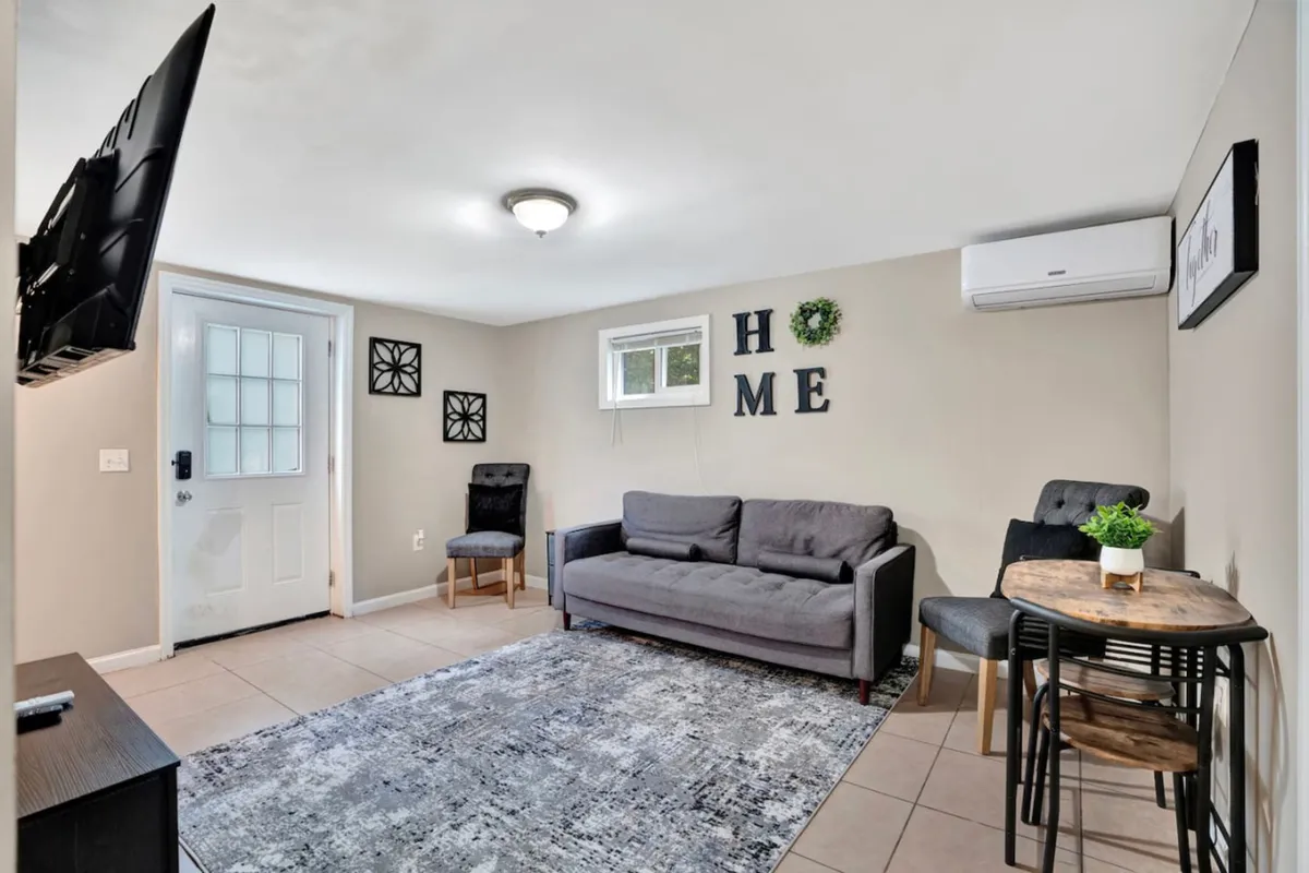 A snug living room featuring a plush sofa, a small dining table, TV, and decorative wall letters, all arranged to encourage relaxation and intimate socializing. The ambiance is cozy and welcoming, ideal for both entertaining and quiet moments.